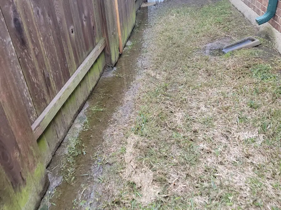 A narrow side yard between a wood fence and a brick wall