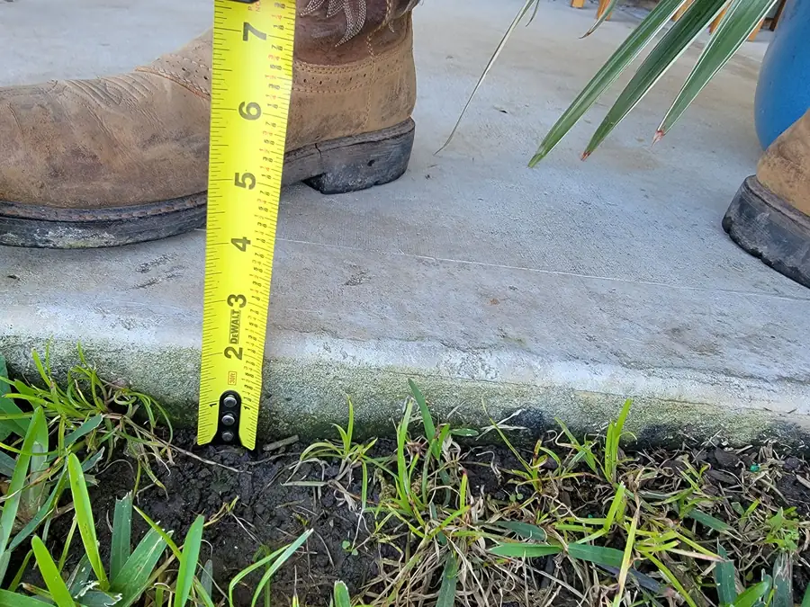 Tape measure held at the edge of a concrete slab showing the soil level