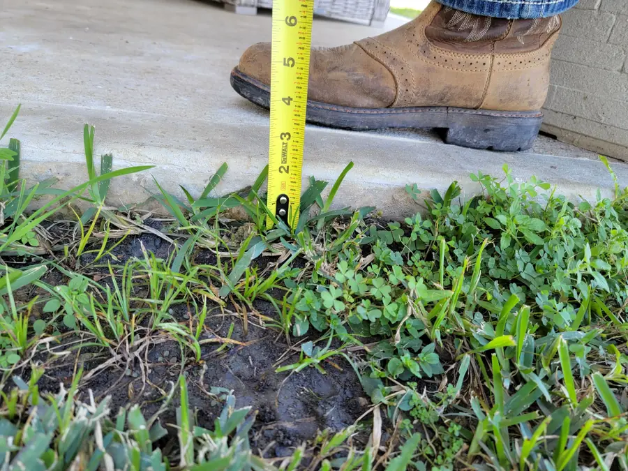 A tape measure held at the edge of a concrete slab to check the grade of the ground